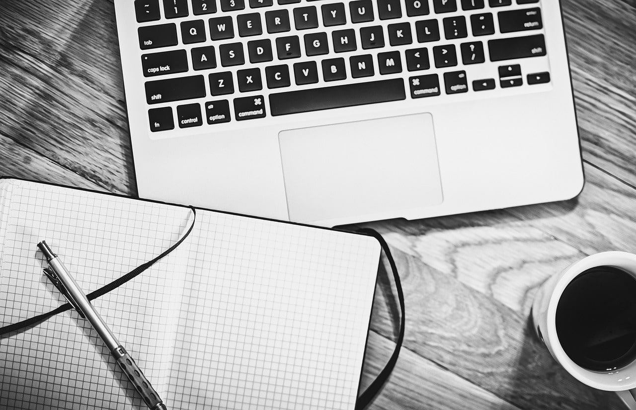 Laptop, Notizbuch und Stift auf einem Holztisch – Planungsphase einer Veranstaltung