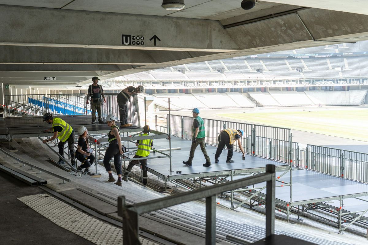 Crew mit Helmen und Warnwesten baut eine Bühne in einem Stadion auf – Symbolbild für SiGeKo bei Veranstaltungen